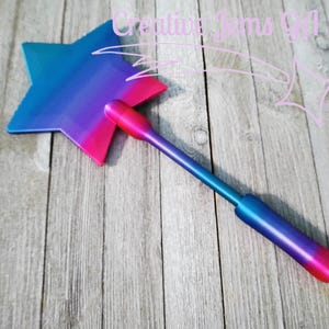 Peut inclure: Une baguette magique en forme d'&eacute;toile avec un d&eacute;grad&eacute; de bleu, de violet et de rose. La baguette a une longue poign&eacute;e et est pos&eacute;e sur un fond en bois. Le texte "Creative Jams Girl" est dans le coin sup&eacute;rieur droit.