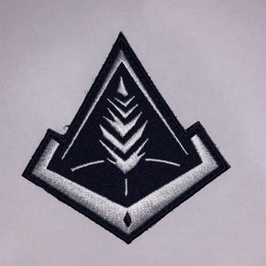 May include: A black and white embroidered patch with a geometric design. The patch features a stylized tree with a diamond shape at the bottom.