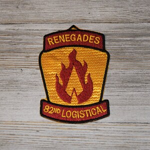 May include: A yellow and red embroidered patch with the words "Renegades 82nd Logistical" and a stylized flame design.