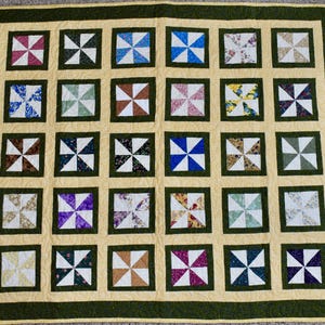 May include: A handmade quilt with a pinwheel design. The quilt features a light yellow background with dark green borders. Each square contains a pinwheel pattern in various colors, including red, blue, green, and purple. The quilt is a patchwork design.