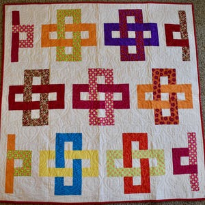 May include: A handmade quilt with a white background and a repeating pattern of interlocking rectangles in various colors. The rectangles are red, orange, purple, pink, yellow, and green, with patterned and solid fabrics. The quilt has a red border.