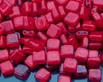 May include: A collection of glossy, square-shaped red beads. The beads have rounded corners and a slightly translucent appearance, with a deep, rich color. The beads are scattered, creating a textured surface.