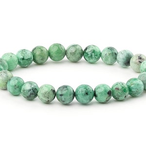May include: A stretch bracelet featuring round, polished beads in shades of green and gray. The beads have a mottled appearance, creating a unique pattern. The bracelet is strung on an elastic cord.