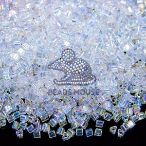 May include: A close-up of a collection of clear, iridescent, rectangular beads. A silver mouse-shaped charm, made of small, round beads, sits amongst them. The beads are scattered on a black surface.