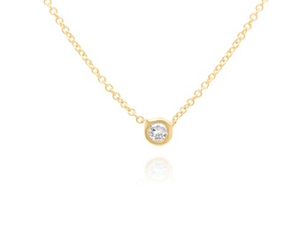 Può includere: Una delicata collana a catena d'oro con un ciondolo rotondo in pietra trasparente.