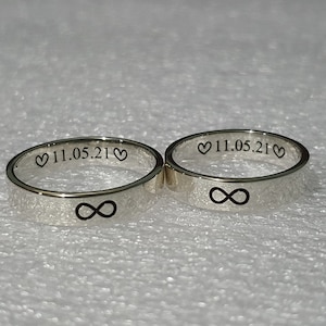 Peut inclure: Deux bagues en argent avec un symbole d'infini gravé sur chacune. Les bagues portent également la date "11.05.21" et un symbole de cœur gravé à l'intérieur.