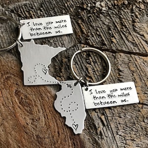 May include: Two silver keychains shaped like the state of Minnesota with the text "I love you more than the miles between us." on each keychain.