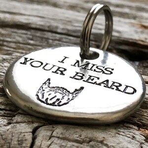 May include: Silver keyring with a round tag that says "I miss your beard" with a beard graphic.