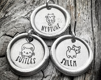 Op de afbeelding: Drie zilveren katten-thema hondenpenningen met de namen "Neptune", "Butters" en "Salem" gegraveerd.
