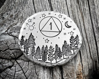 May include: A silver circular pendant with an engraved design of a triangle with a circle inside, containing the number "1". The design is surrounded by stars and a crescent moon. The bottom of the pendant features a row of stylized trees.