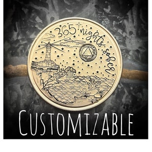 May include: Gold-toned round coin with a black and white design of a lighthouse, waves, and stars. The text "365 nights sober" is inscribed around the edge of the coin.
