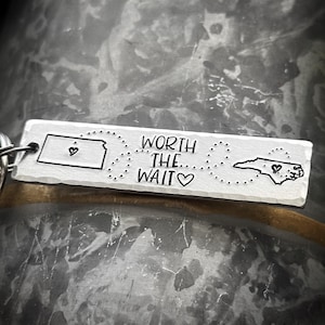 May include: A silver keychain with an outline of Kansas and North Carolina, connected by a dotted line. The text "WORTH THE WAIT" is engraved on the keychain, with a heart symbol after "WAIT".