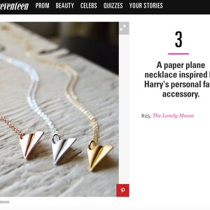 May include: Three paper airplane necklaces in rose gold, silver, and gold. Each necklace features a delicate chain and a folded paper airplane pendant. The necklaces are displayed on a light-colored wooden surface.