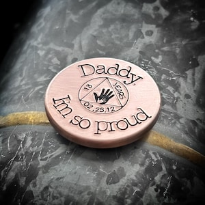 K&ouml;nnte beinhalten: Eine runde M&uuml;nze aus Kupfer mit den Worten "Daddy I'm so proud" eingraviert am Rand. In der Mitte befindet sich ein Dreieck mit den Worten "13 Years" und dem Datum "02.25.12" im Inneren.