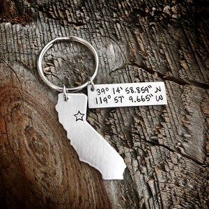 May include: Silver keychain with a cutout of the state of California and coordinates engraved on a tag: "39&deg; 14' 58.859" N 119&deg; 57' 9.665" W"