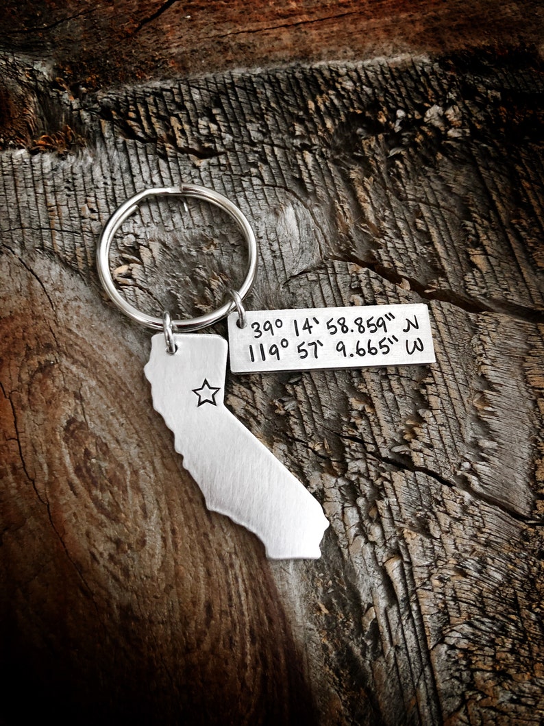 May include: Silver keychain with a cutout of the state of California and coordinates engraved on a tag: "39&deg; 14' 58.859" N 119&deg; 57' 9.665" W"