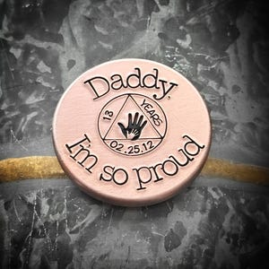 K&ouml;nnte beinhalten: Eine ros&eacute;goldene Metallm&uuml;nze mit dem Text "Daddy, I'm so proud" und einem Dreieck mit dem Text "13 Years" und dem Datum "02.25.12" darin.