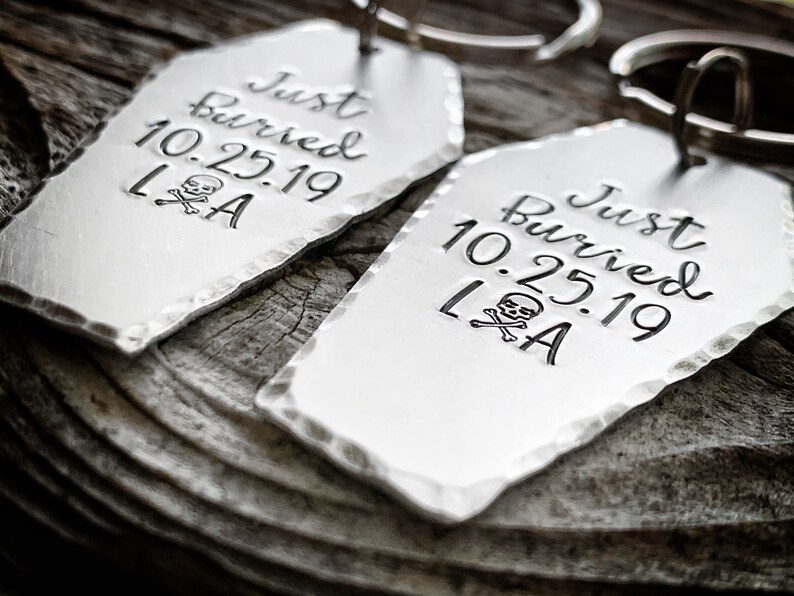 May include: Two silver coffin-shaped keychains with the text "Just Buried 10.25.19 LA" and a skull and crossbones graphic.
