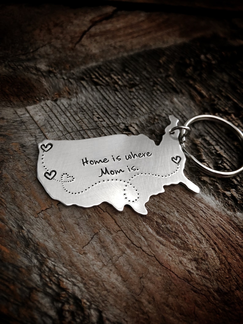 Puede incluir: Un llavero de plata con forma de Estados Unidos con el texto "Home is where Mom is" y una l&iacute;nea punteada con corazones a lo largo del borde.