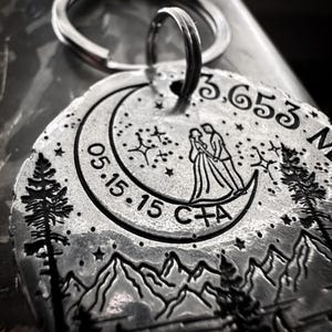 May include: Silver keychain with a crescent moon design, a couple standing on the moon, and the date 05.15.15. The keychain also includes the text "C+A" and the coordinates 3.653 N.