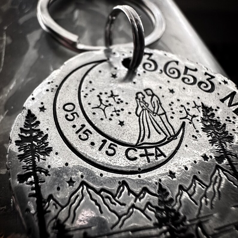 May include: Silver keychain with a crescent moon design, a couple standing on the moon, and the date 05.15.15. The keychain also includes the text "C+A" and the coordinates 3.653 N.