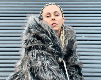 May include: A woman wearing a black and white faux fur jacket with a hood. She is wearing a black top and black pants. The jacket has a long, shaggy fur.