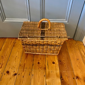 May include: A woven wicker basket with a brown handle. The basket has a dark brown stripe pattern on the lid and sides.