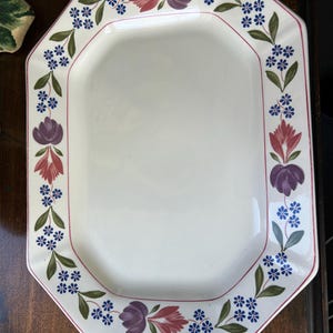 May include: An octagonal white serving platter with a floral border. The border features purple, red, and blue flowers with green leaves. A thin red line frames the inner edge of the platter.
