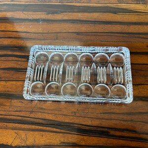 May include: A rectangular, clear glass serving tray with a decorative pattern of circles and vertical lines. The tray is designed with multiple compartments, ideal for serving appetizers or small portions. The glass has a textured appearance.