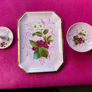 May include: A set of three vintage porcelain serving pieces. The set includes a rectangular tray with gold trim, a small round dish, and a small round dish with a decorative figurine. All pieces are light pink with floral designs.