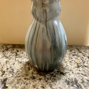 May include: A grey and white ceramic vase with a wavy, organic shape. The vase has a marbled glaze with streaks of grey, white, and brown.