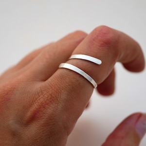 May include: A silver ring with a simple, minimalist design. The ring is made of a single, thin band of metal that wraps around the finger twice.