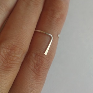 May include: A simple silver ring with a straight band and a small, rounded end. The ring is worn on a finger.
