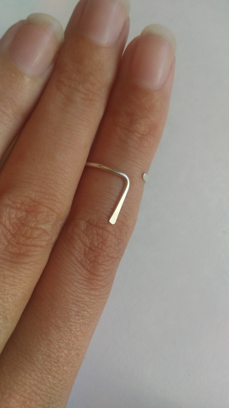 May include: A simple silver ring with a straight band and a small, rounded end. The ring is worn on a finger.