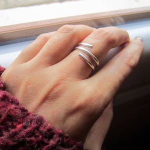 May include: A silver ring with three bands twisted together. The ring is worn on a person's finger.