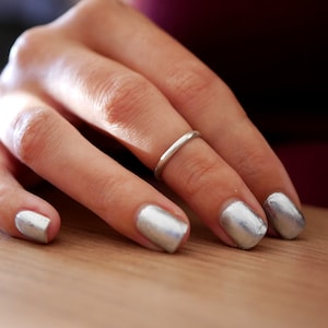 Peut inclure: Une main avec du vernis à ongles argenté sur les ongles. L'annulaire porte une fine bague argentée.