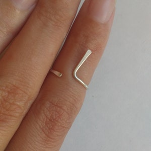 May include: A silver ring with a simple, minimalist design. The ring is made of a single piece of metal that is bent into a V-shape.