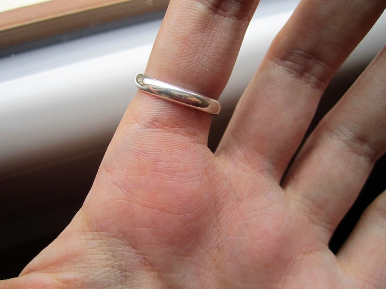 May include: A silver band ring worn on a finger.