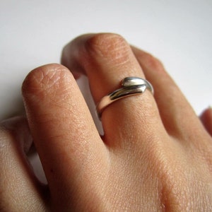 May include: A silver ring with a unique, twisted design. The ring is worn on a person's finger.