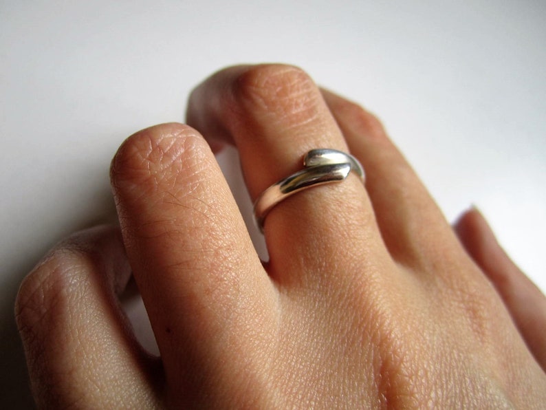 May include: A silver ring with a unique, twisted design. The ring is worn on a person's finger.