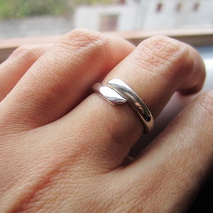 May include: A silver ring with a unique, angular design. The ring is worn on the index finger of a hand.
