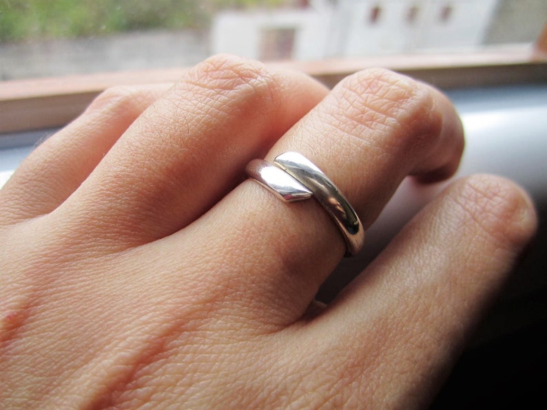 May include: A silver ring with a unique, angular design. The ring is worn on the index finger of a hand.