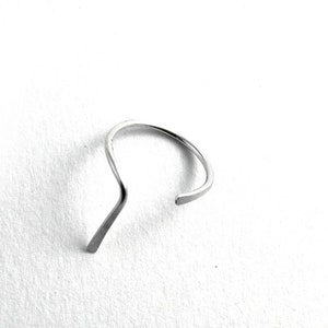 May include: A silver ring with a unique, curved design. The ring is made of a single piece of metal that is bent into a shape that resembles a wave.