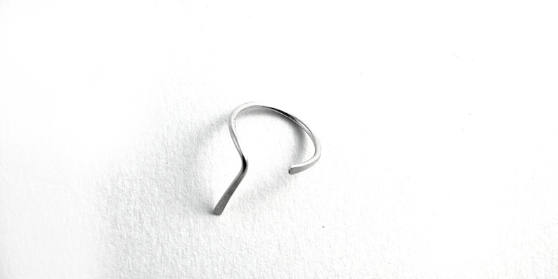 May include: A silver ring with a unique, curved design. The ring is made of a single piece of metal that is bent into a shape that resembles a wave.