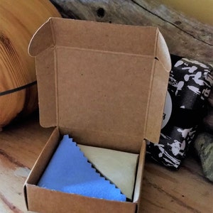 May include: A small, brown cardboard box with a blue and white cleaning cloth inside. The box is open and the cloth is visible.