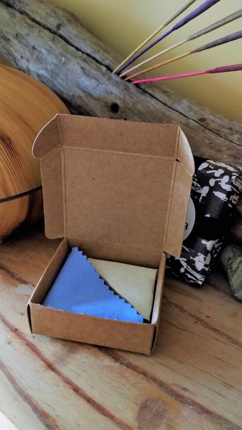 May include: A small, brown cardboard box with a blue and white cleaning cloth inside. The box is open and the cloth is visible.