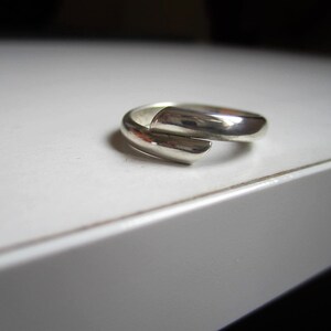 May include: A silver ring with a unique, twisted design. The ring is made of a single piece of metal that is bent and twisted to create a unique shape.