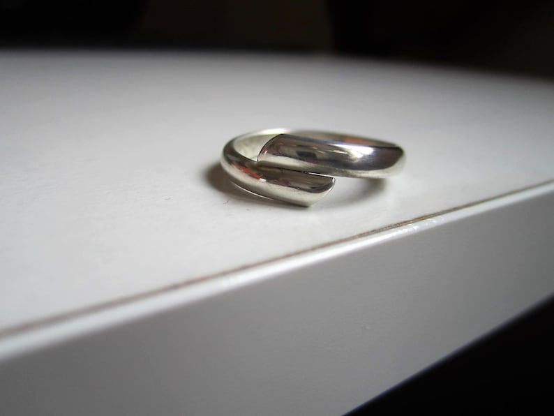 May include: A silver ring with a unique, twisted design. The ring is made of a single piece of metal that is bent and twisted to create a unique shape.
