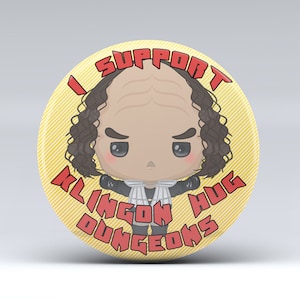 May include: A yellow button with the text "I Support Klingon Hug Dungeons" in red. A cartoon illustration of a person with brown hair and a serious expression is in the center.