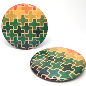May include: Two round, colorful buttons with a geometric pattern of green, yellow, orange, and red squares. The buttons have a glossy finish.
